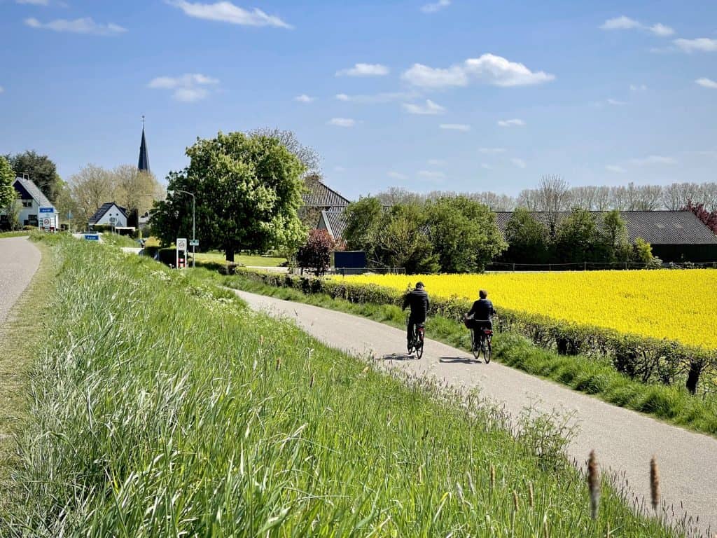 Fietsers genieten van het landschap op 't Gelders Eiland met groene velden en een pittoresk dorpje o.