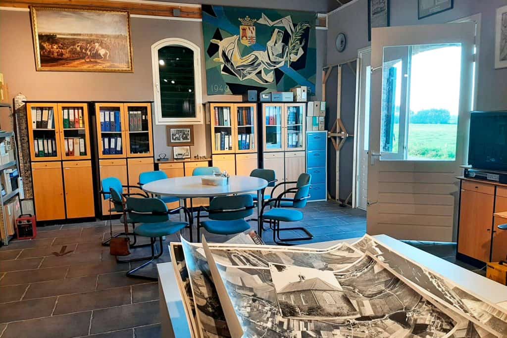 Interieur van een historisch archief met boeken, foto's en een tafel.