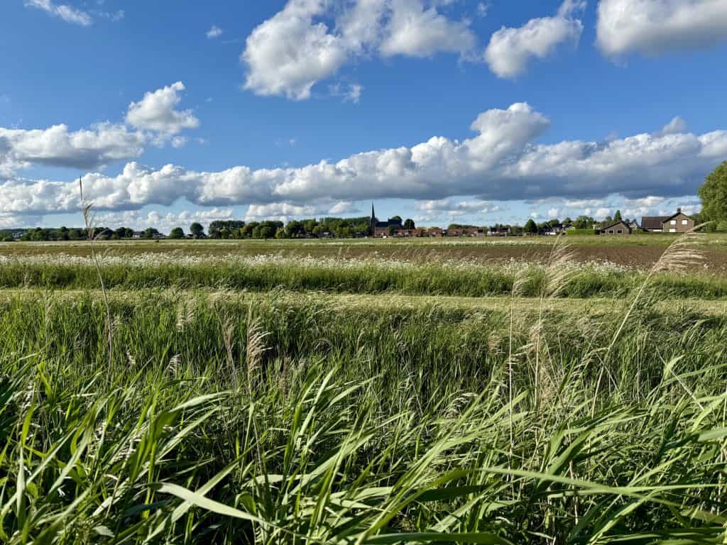 Gelders Eiland landschap met groene velden, wolken en een dorp op de achtergrond.