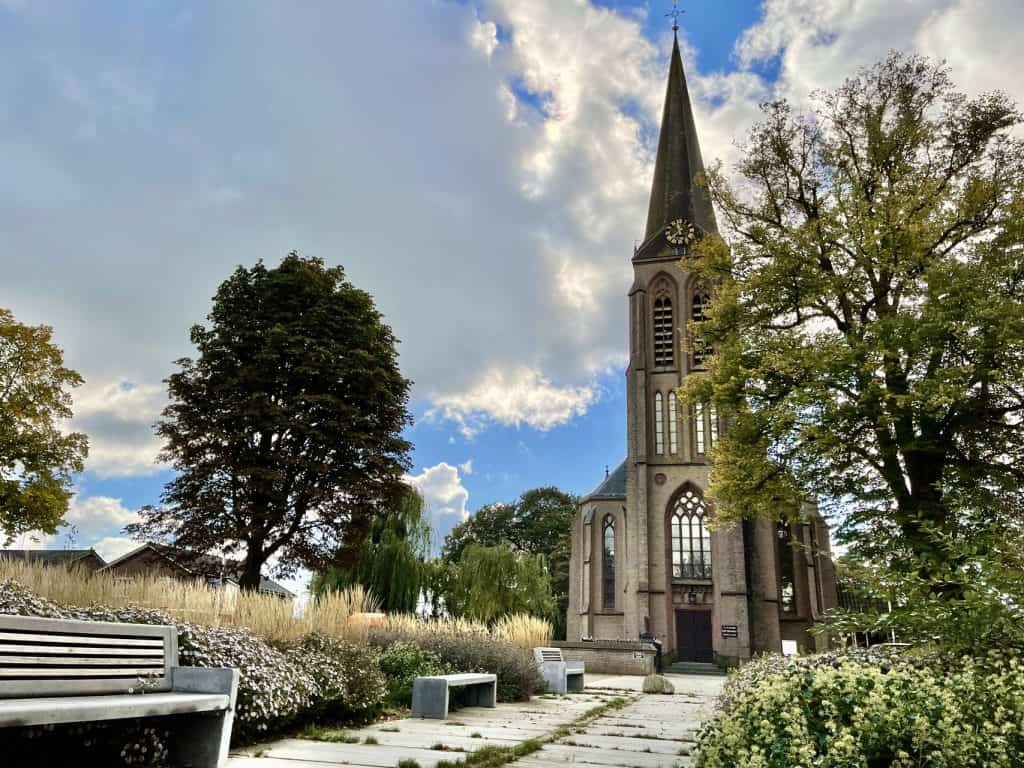 Kerk op 't Gelders Eiland met tuin, bomen en een heldere hemel.