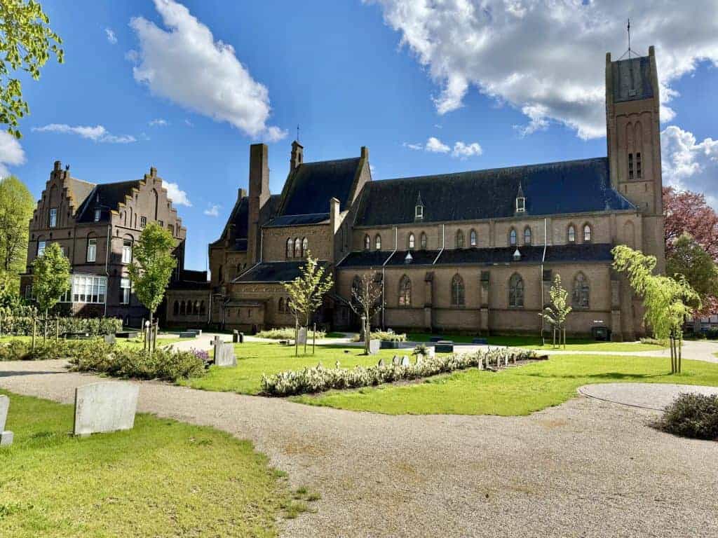 Kerk op 't Gelders Eiland met groene tuin en wandelpaden onder een blauwe hemel.