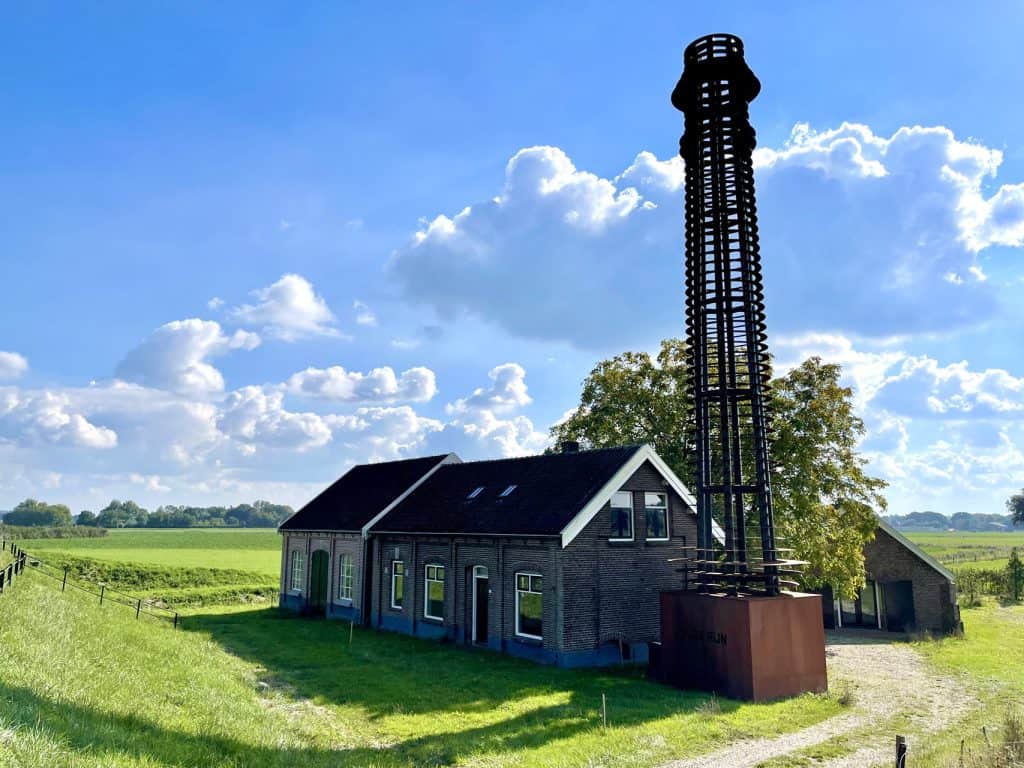 Historische vuurtoren en huis op 't Gelders Eiland, omgeven door groene velden.