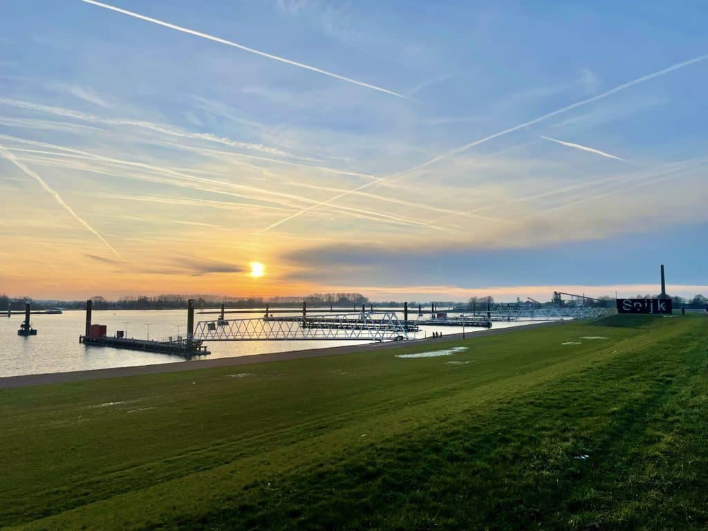 Zonsondergang over de rivier met grasveld en schepen op 't Gelders Eiland.
