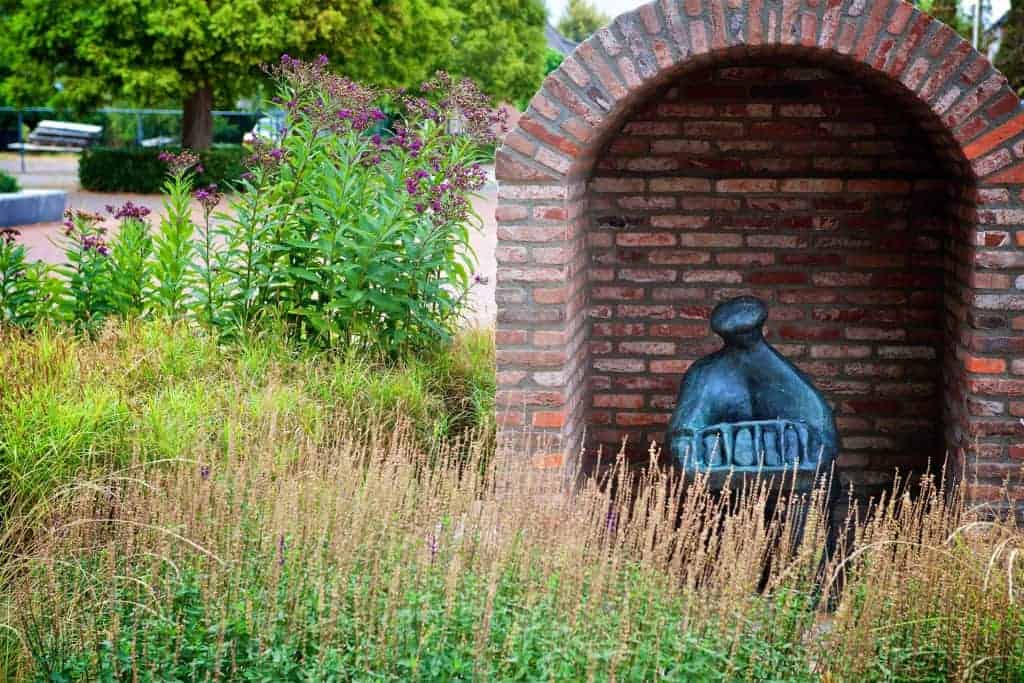 Beeld van een monument in een tuin op 't Gelders Eiland, omgeven door bloemen en planten.
