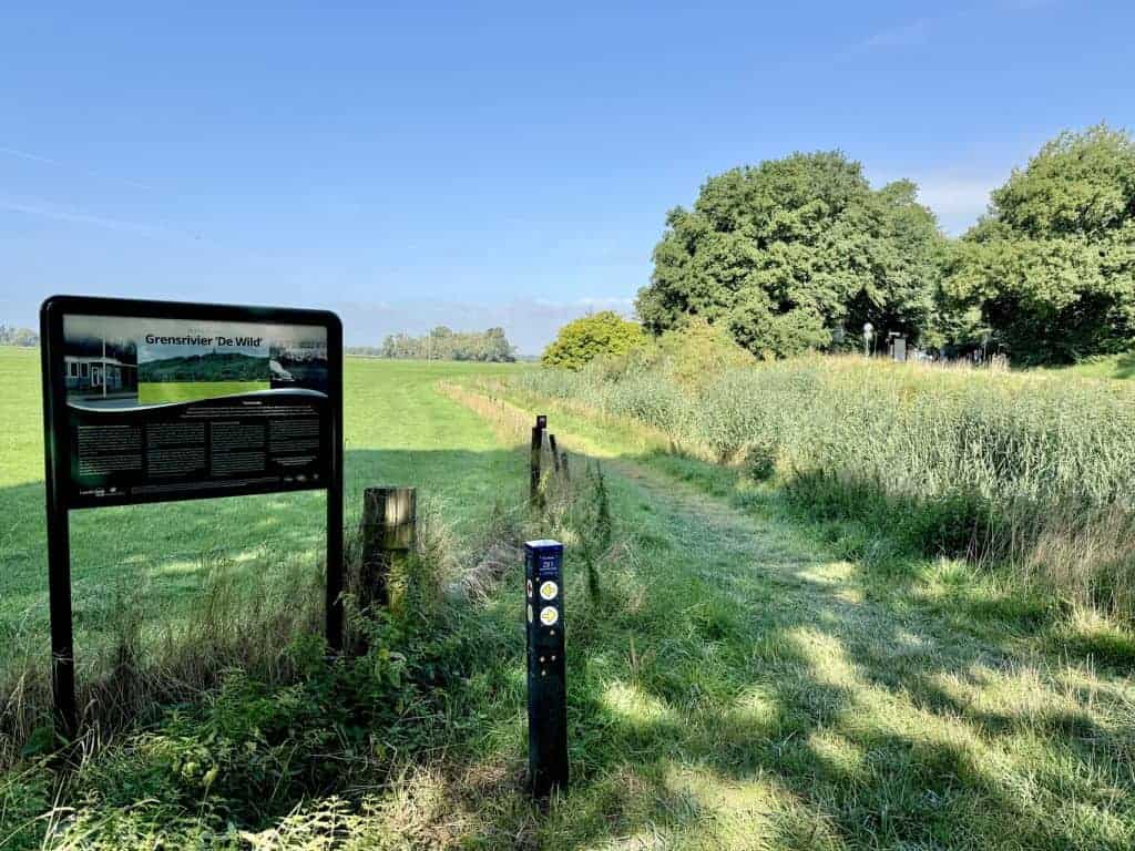 Informatiebord over de grens tussen Nederland en België op 't Gelders Eiland, omgeven door groene ve.
