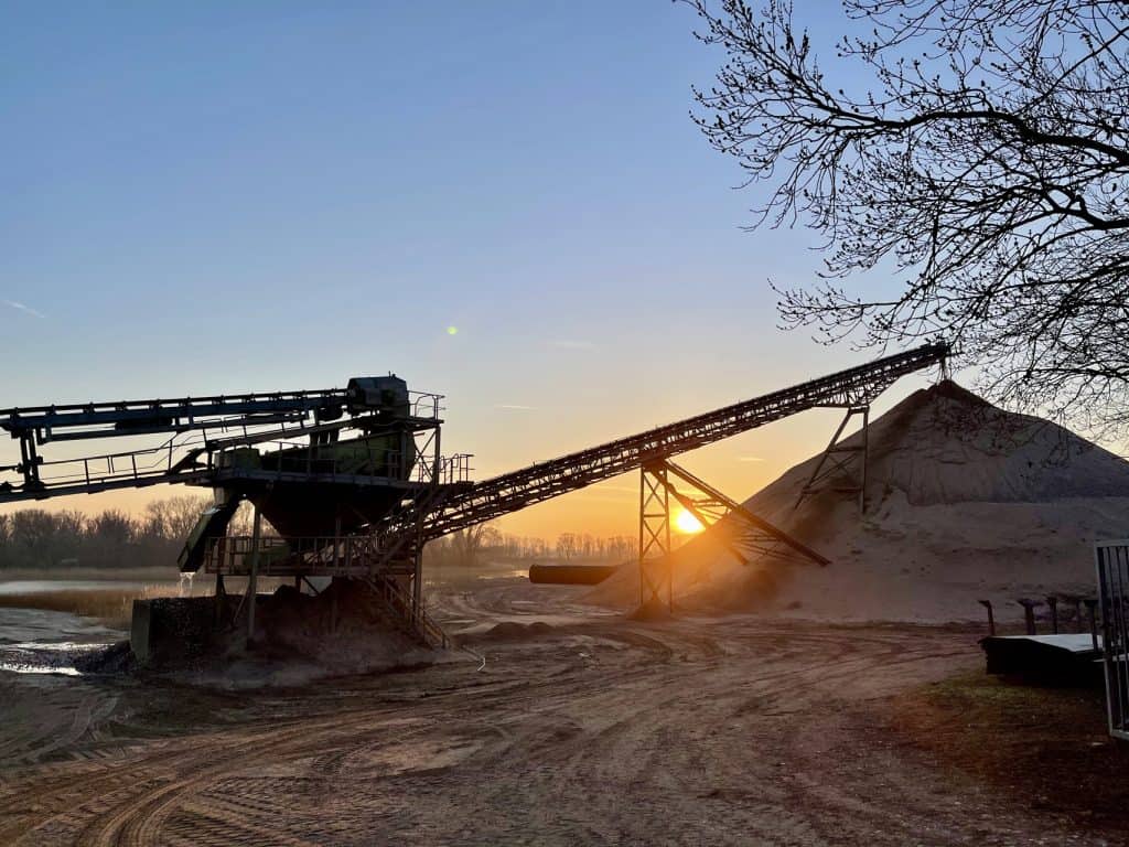 Zandwinning op 't Gelders Eiland tijdens zonsondergang met industriële machines.