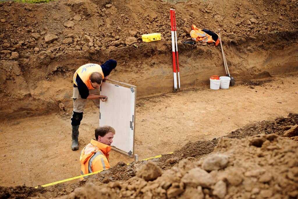 Archeologen werken aan opgraving op 't Gelders Eiland, met meetinstrumenten en meetlint.