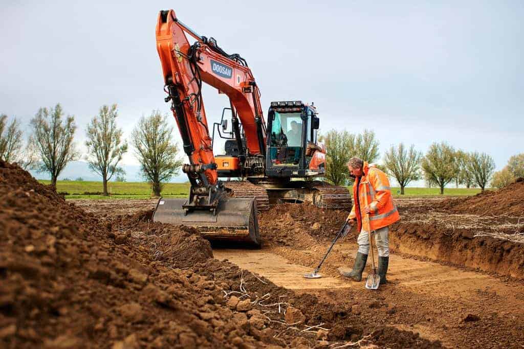 Archeoloog en graafmachine op 't Gelders Eiland, bezig met opgravingen en bodemonderzoek in een open.