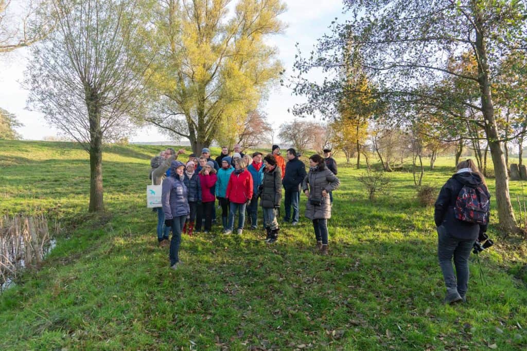 Gezelschap wandelaars op 't Gelders Eiland in de natuur, herfstkleuren en groene velden.