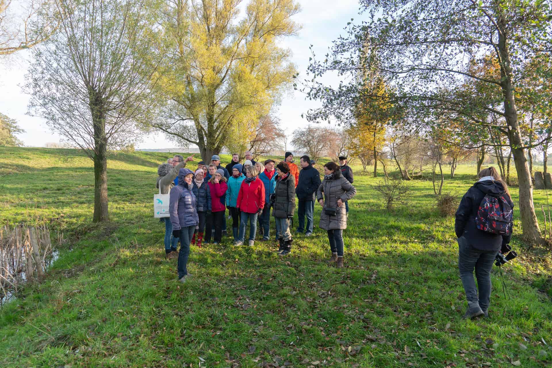 Gezelschap wandelaars op 't Gelders Eiland in de natuur, herfstkleuren en groene velden.