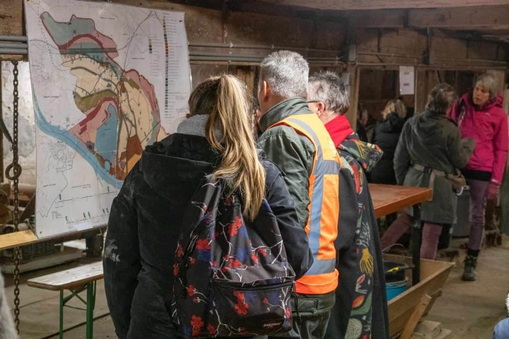 Gezellige groep mensen bekijkt een kaart op 't Gelders Eiland, in een informatieve en rustieke omgev.