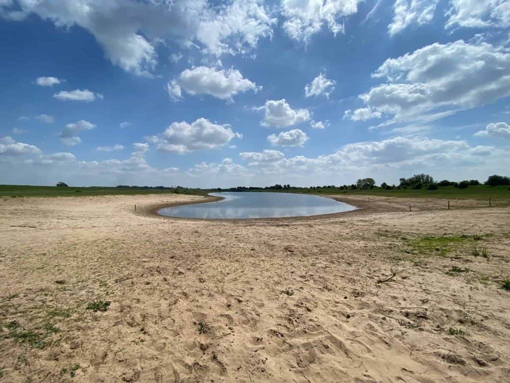 Zandvlakte met klein waterpoel op 't Gelders Eiland onder een bewolkte hemel.