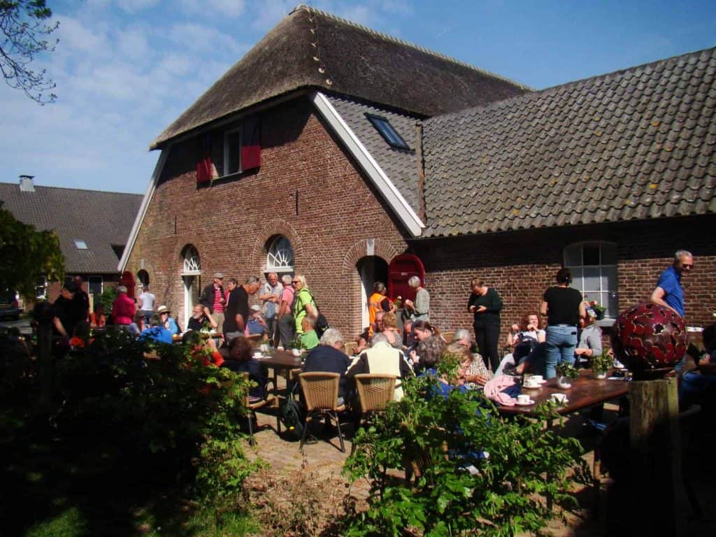 Gezellige buitenbijeenkomst op 't Gelders Eiland met mensen en tafels in een tuin.