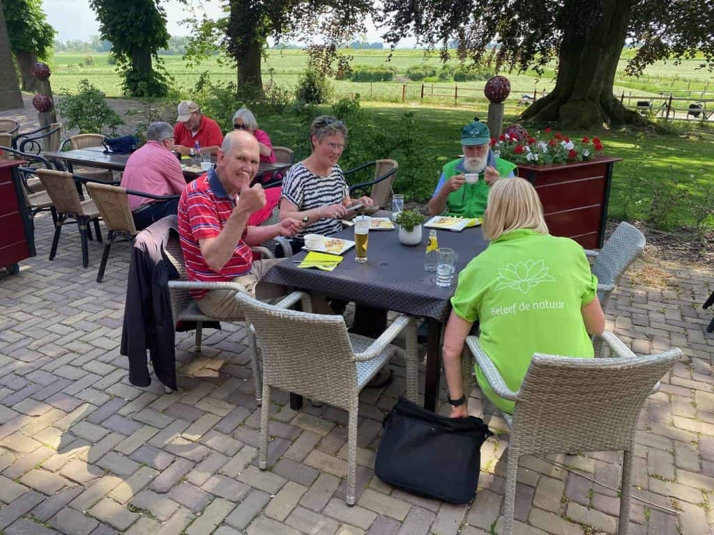 Gezellige groep mensen geniet van een maaltijd op een terras op 't Gelders Eiland, omgeven door groe.