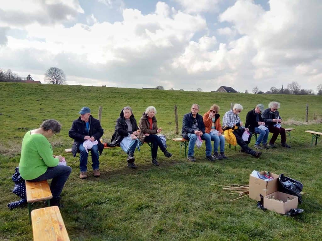 Groep mensen zit op bankjes in een groen landschap op 't Gelders Eiland.