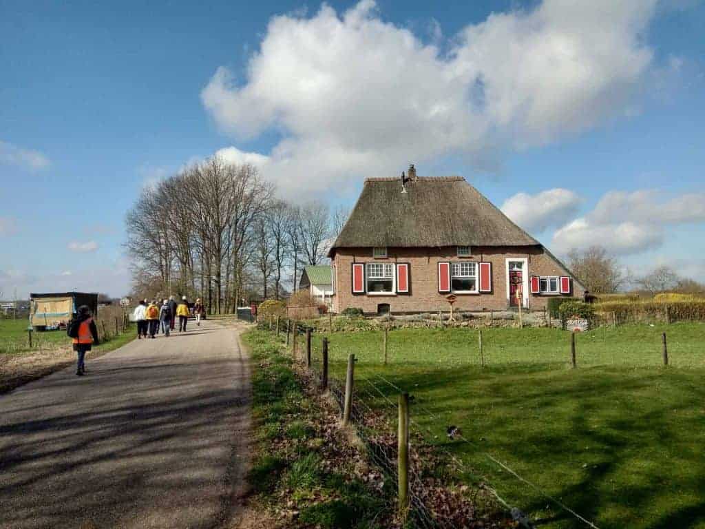 Kleurrijk huis op 't Gelders Eiland met wandelende mensen en groene omgeving onder een blauwe hemel.