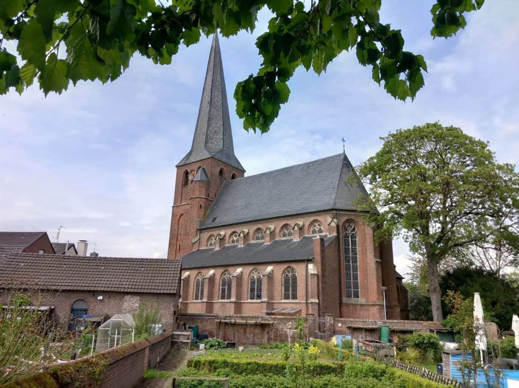 Kerk op 't Gelders Eiland met hoge toren en omliggende tuin, onder een blauwe hemel met groene bomen.