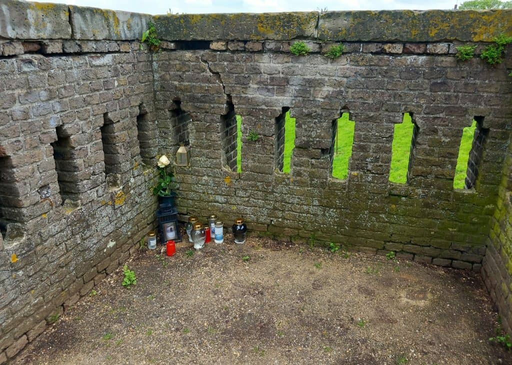 Kerkmuur met grafstenen en bloemen op 't Gelders Eiland, historische begraafplaats.
