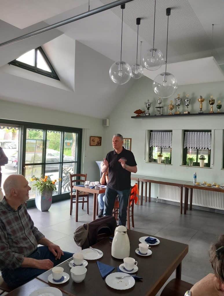 Kleine groep mensen in een lichte, moderne eetkamer met grote ramen en hangende glazen lampen.
