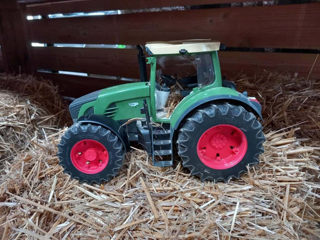 Een speelgoedtractor op strooisel in een schuur of stal.