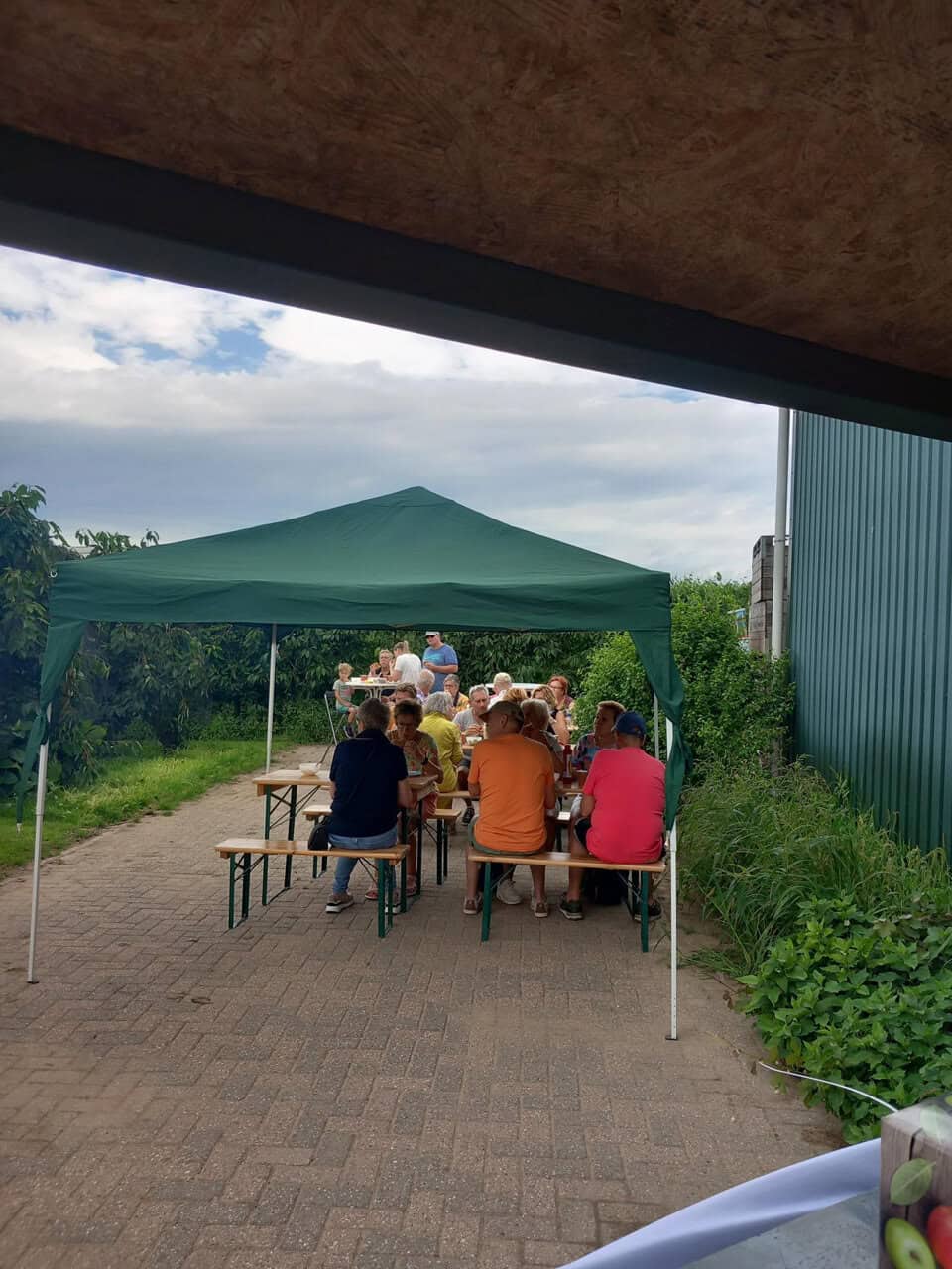 Gezellige groep mensen onder een groene tent op 't Gelders Eiland, genietend van een buitenmaaltijd.