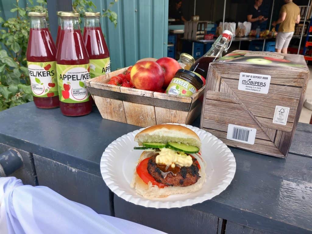 Appelcider, verse appels en een hamburger met groenten op een tafel op 't Gelders Eiland.