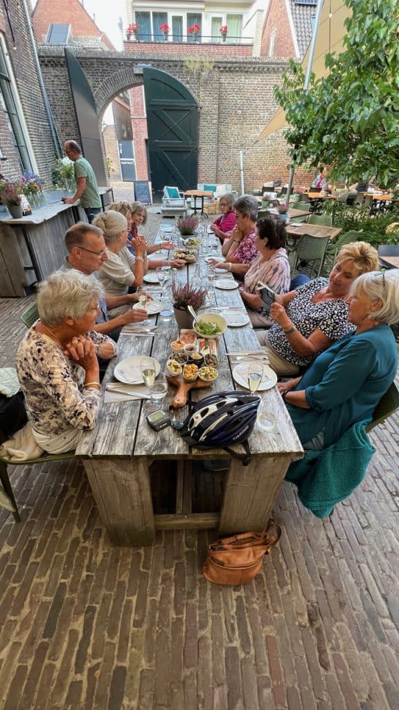 Gezellig groepje ouderen geniet van een gezamenlijke maaltijd in een sfeervolle binnenplaats op 't G.