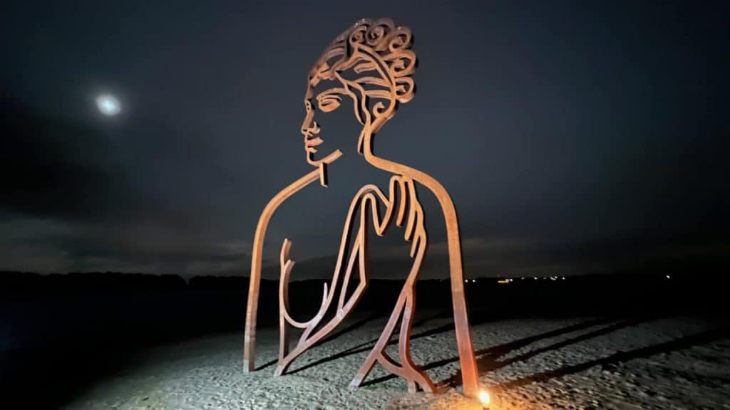 Kunstwerk van een grote vrouwenfiguur op 't Gelders Eiland bij nacht.