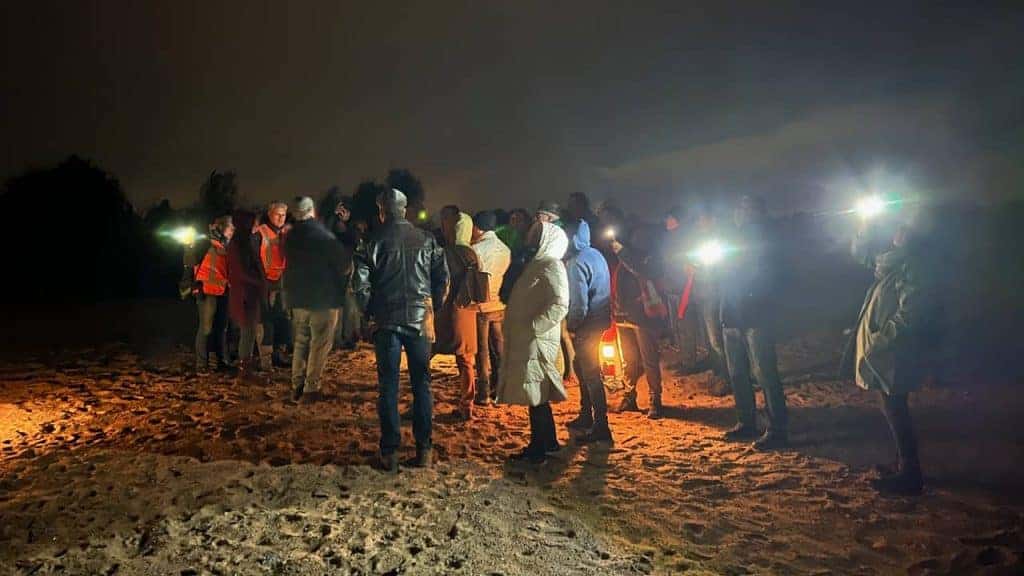 Lichtshow op ’t Gelders Eiland met mensen bij nacht op het strand.