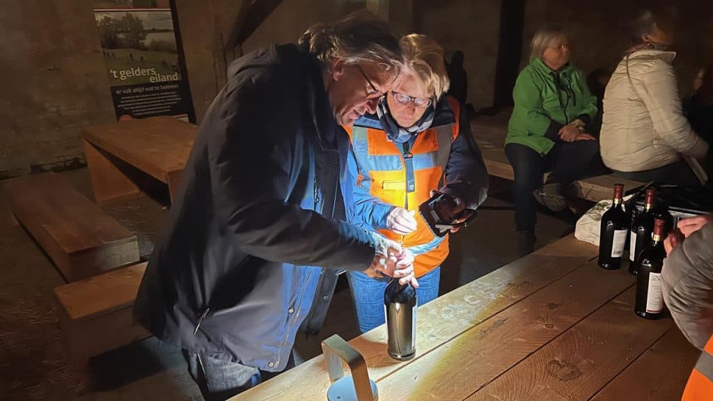 Een groep mensen geniet van een wijnproeverij op 't Gelders Eiland, met gezellige sfeer en mooie omg.