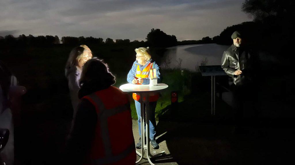 Lichtshow op 't Gelders Eiland bij zonsondergang met mensen en een waterkant.