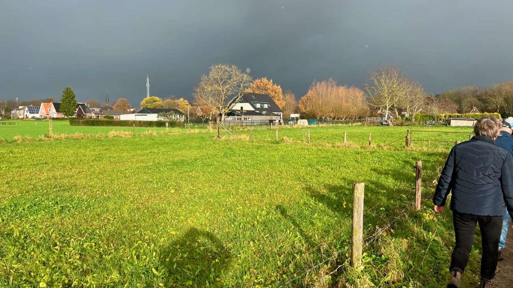 Zonnige dag op 't Gelders Eiland met groene velden en donkere wolken op de achtergrond.