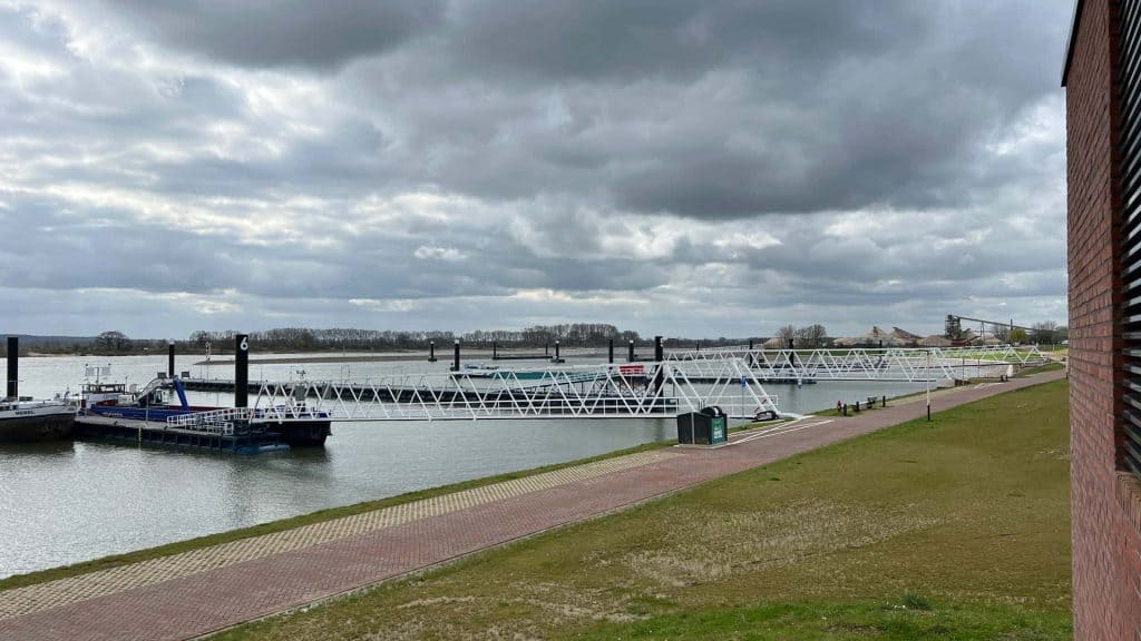 Zicht op de haven en de rivier op 't Gelders Eiland met boten en een wandelpad onder een bewolkte he.