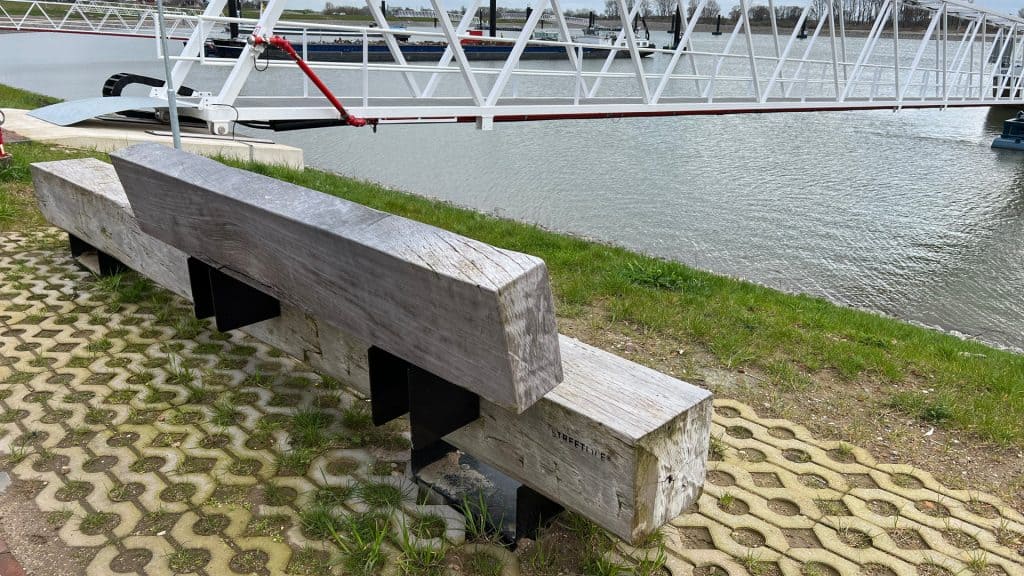 Zweeds houten bank aan het water op 't Gelders Eiland, met boten en een pier op de achtergrond.