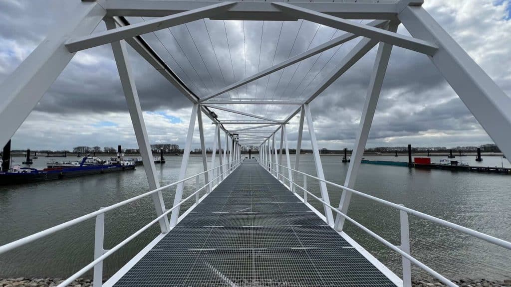 Zweefbrug over water op 't Gelders Eiland met wolkenlucht, moderne structuur en boten op de achtergr.