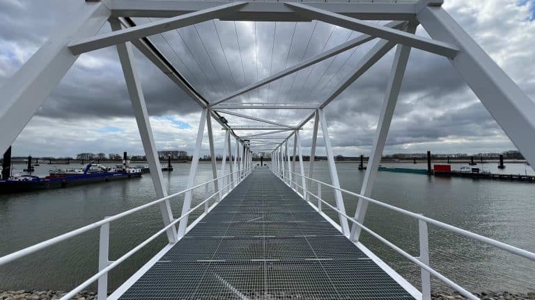 Zweefbrug over water op 't Gelders Eiland met wolkenlucht, moderne structuur en boten op de achtergr.