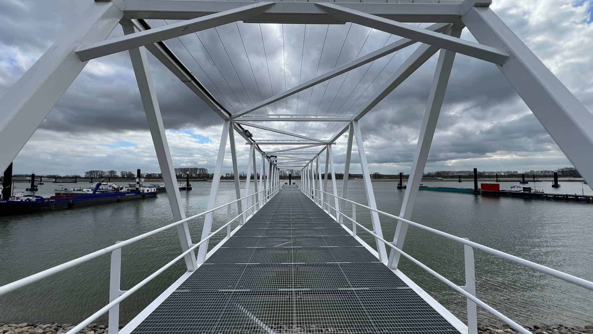 Zweefbrug over water op 't Gelders Eiland met wolkenlucht, moderne structuur en boten op de achtergr.