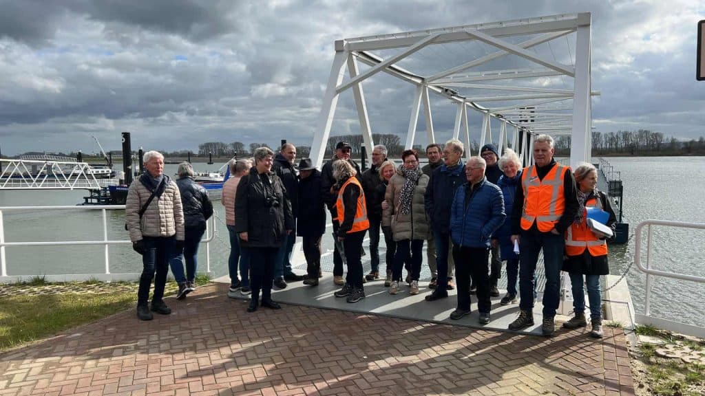 Haven op 't Gelders Eiland met groep toeristen en gids bij brug over rivier, mooie dag, water en bot.