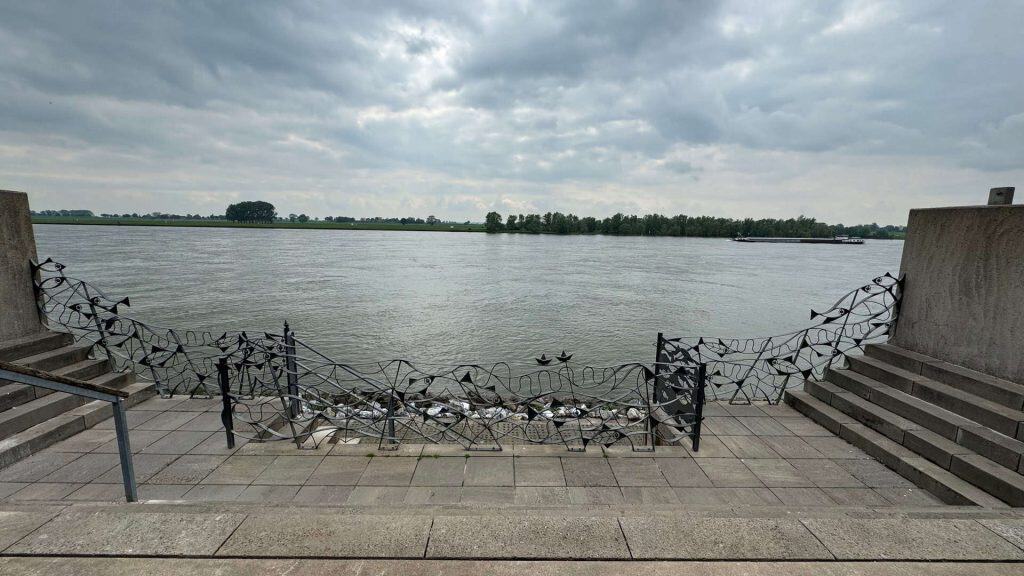 Rustige rivierzicht op 't Gelders Eiland met steiger en waterkant onder bewolkte hemel.
