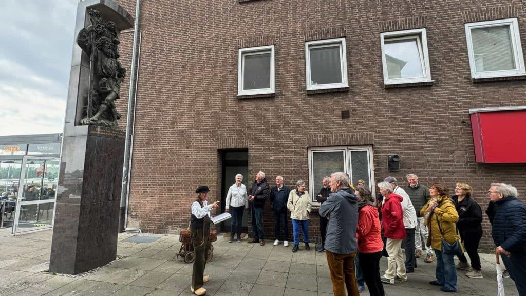 Historische gids geeft uitleg aan groep toeristen bij 't Gelders Eiland, met een beeldhouwwerk en ee.