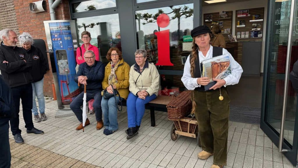 Gezellige groep mensen wacht buiten een winkel op 't Gelders Eiland, terwijl een vrouw met boeken zi.
