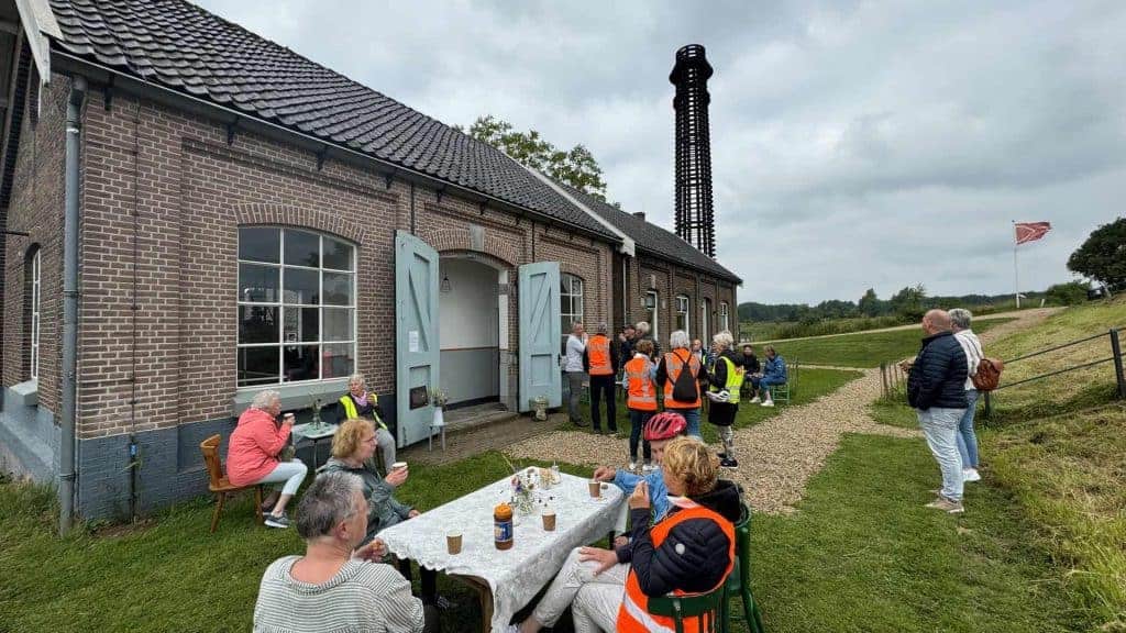 Kleine groep mensen bij historisch gebouw op 't Gelders Eiland, met uitzicht op landschap en windmol.