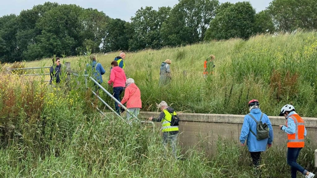 Leden verzamelen zich langs de oever van 't Gelders Eiland voor een natuur- en milieuproject.