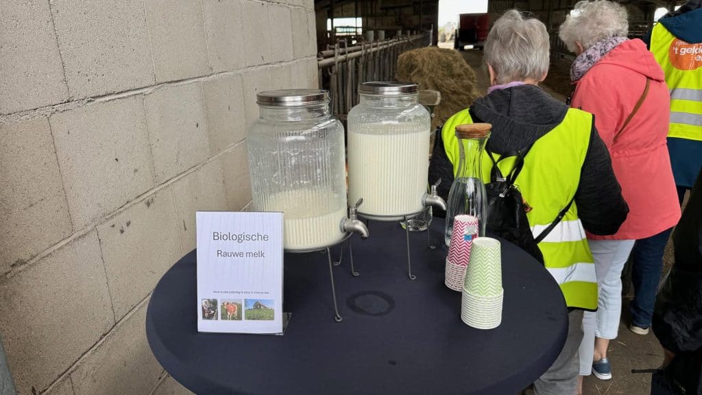 Biologische rauwe melk in glazen jerrycans op 't Gelders Eiland, bezoekers genieten van verse zuivel.