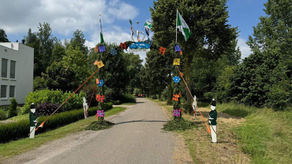 Kleurrijk feestpoortje met vlaggen en bloemen op 't Gelders Eiland, omgeven door groene bomen en een.