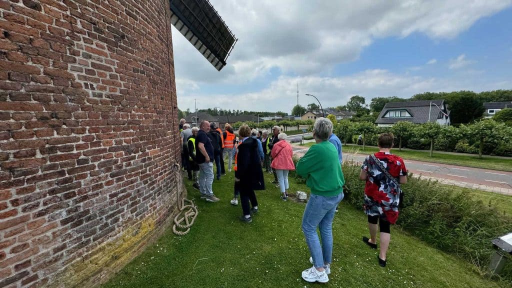 Kleine groep mensen bij een historische windmolen op ’t Gelders Eiland, Nederland, in een groene omg.