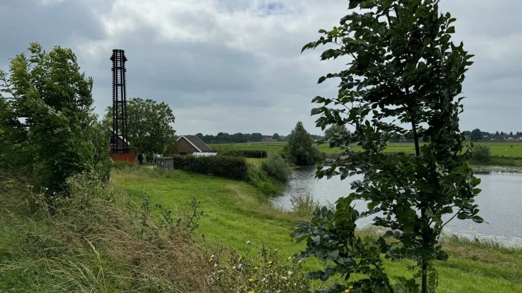 Zicht op de rivier en groene weilanden op 't Gelders Eiland, met een molen en een boerderij in de ac.