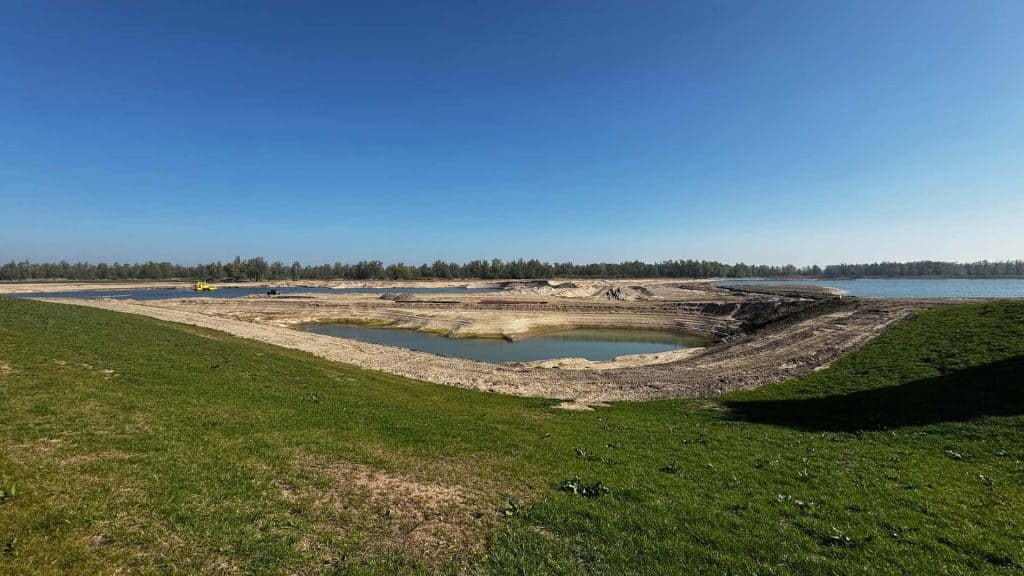 Zandafgraving op 't Gelders Eiland met waterpartijen en groene grasvelden onder een heldere blauwe h.