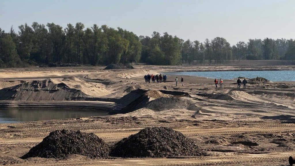 Zandstrand en groep wandelaars op 't Gelders Eiland, met water en bos in de achtergrond.