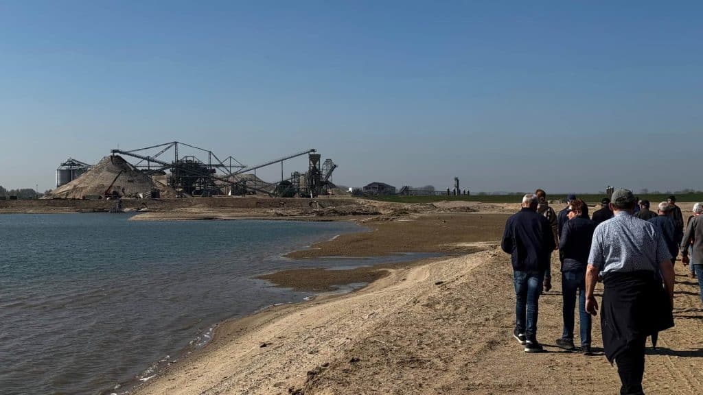 Groep mensen wandelt langs de rivier op 't Gelders Eiland met industriële achtergrond.
